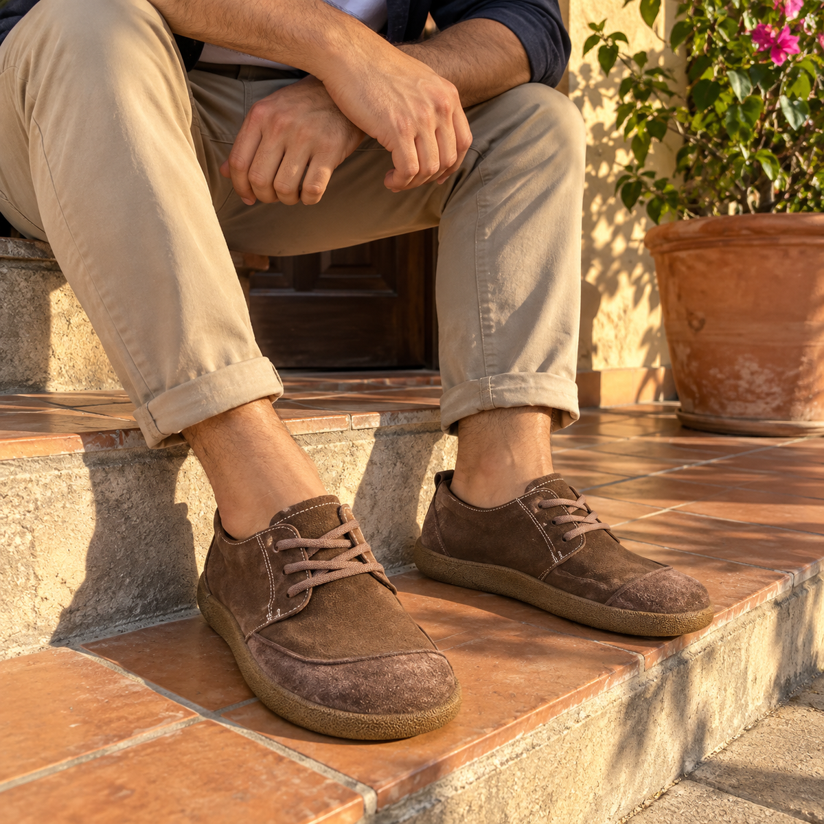 Hombre con chinos y zapatos marrón sentado en la entrada de su casa